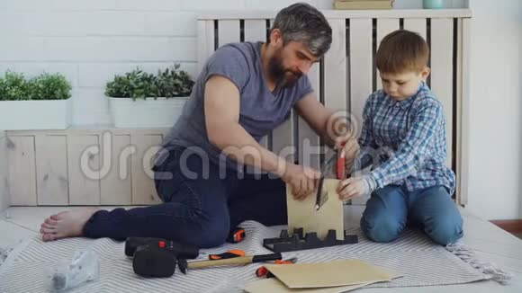 大胡子的父亲和小可爱的儿子在家里用木床单做鸟舍儿童和父母观念视频的预览图