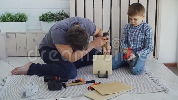 有帮助的儿子正在用手锯锯木片而他的父亲正在用量筒锯锯木片并与他交谈视频的预览图