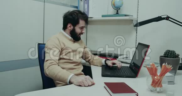 办公室工作人员坐在他的桌子上在笔记本电脑上工作疲惫而紧张地打着电话视频的预览图