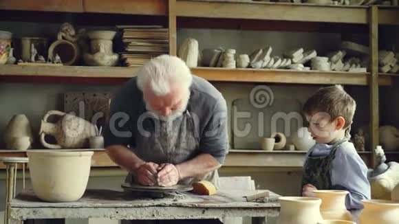 关心的老爷爷正在向小孙子展示如何在小作坊里用粘土做投掷轮陶器视频的预览图