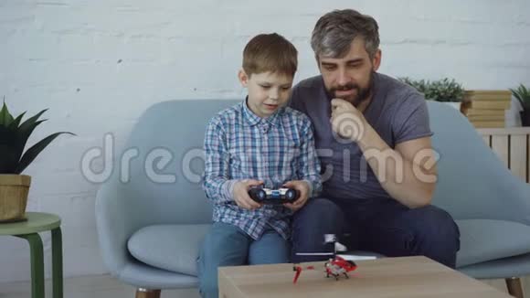 可爱的孩子拿着发射机控制着飞行直升机而他的父亲正试图用他的直升机接住它视频的预览图