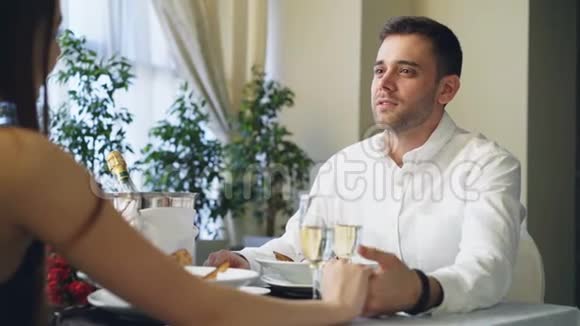 年轻的帅哥正在和他的女朋友握着她的手说话他们正碰着眼镜一边喝着香槟视频的预览图