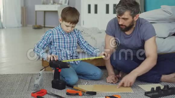 小男孩在和父亲一起做建筑工程时正在学习使用测量卷轴而父亲则在解释视频的预览图