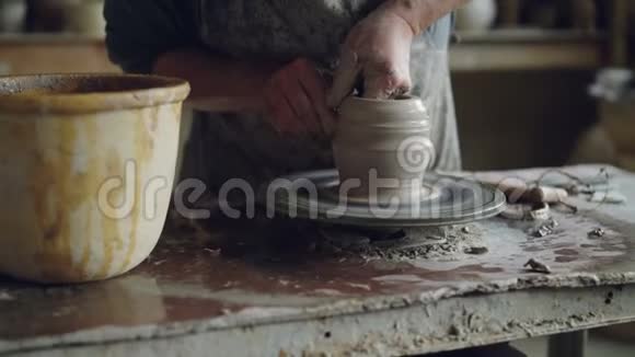 专业陶工的倾斜镜头在工作场所使用投掷轮从棕色粘土中制造罐子传统陶器视频的预览图