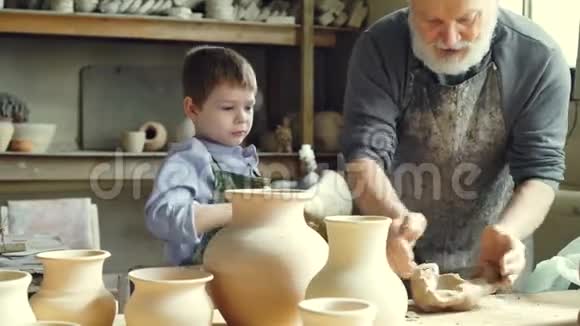 经验丰富的男性陶工正在混合和揉捏粘土而他可爱的小孙子正在帮助他在车间陶器视频的预览图
