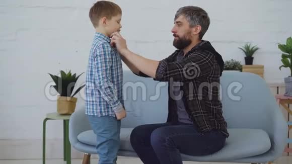小心的父亲正在帮助他的小儿子穿好衣服扣上衬衫抚平头发可爱的父母快乐视频的预览图