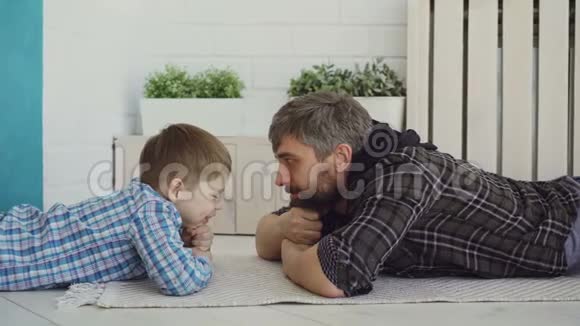 可爱的小孩子和他慈爱的爸爸躺在地板上看着他说话家庭幸福有趣视频的预览图