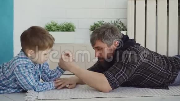 开朗的父亲正在教他的小儿子摔跤给他看手的姿势假装输了男孩是视频的预览图