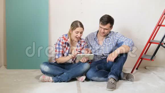 一对年轻夫妇坐在正在装修的公寓地板上在平板电脑上选择家具的4K镜头视频的预览图