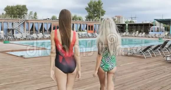 两个美丽的女人在游泳池里走来走去两个女孩在酒店游泳池边摆姿势视频的预览图
