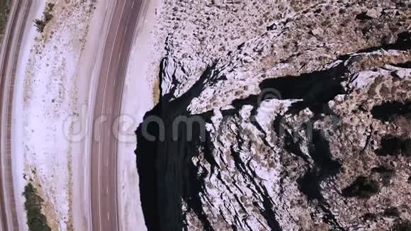 俯视图无人驾驶飞机在美丽的公路公路和铁路上右转靠近史诗般的岩石砂岩山脉视频的预览图