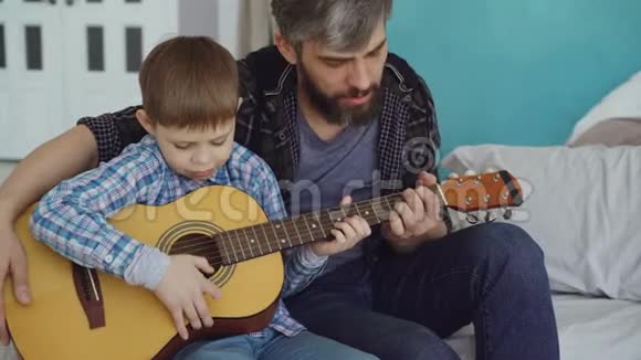 专心致志的孩子正在和他父亲有经验的吉他手弹吉他调整乐器享受音乐视频的预览图