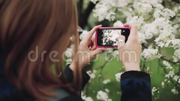 一个在盛开的春天花园里拿着电话的随便女人后景视频的预览图