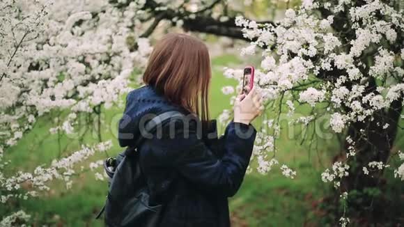 在一个盛开的春天花园里带着电话的休闲时髦女孩视频的预览图