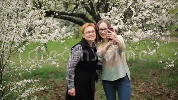 高级母亲和她的成年女儿在盛开的花园里自拍视频的预览图