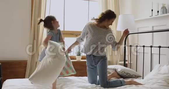 快乐的妈妈和学龄前儿童在床上享受枕头大战视频的预览图