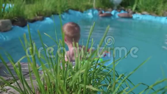 孩子在一个小池塘里的充气圈里游泳园区花草环湖快乐视频的预览图
