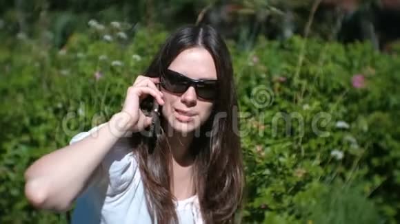 美丽的年轻女子坐在公园里用手机打电话和交谈视频的预览图