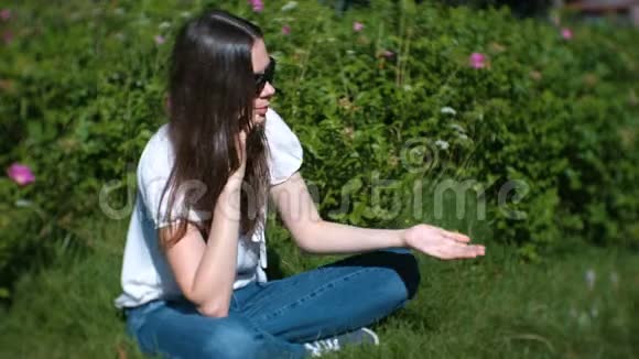 美丽的年轻女子坐在公园里用手机打电话和交谈视频的预览图