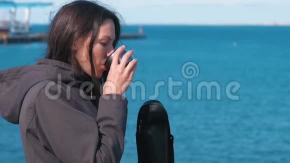 女人在水边用热水瓶喝茶年轻的黑发女人在旅途中视频的预览图