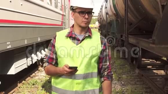 一个戴眼镜戴头盔穿制服的人拿着电话走在火车站的画像视频的预览图