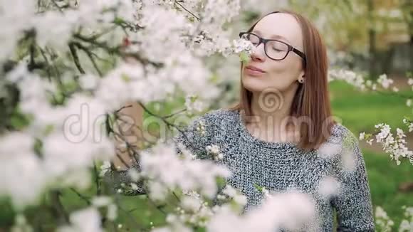 漂亮的戴眼镜的白种人女孩喜欢白色樱花的味道特写镜头视频的预览图