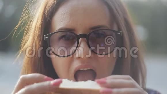 特写镜头一个正在吃新鲜三明治的女孩戴眼镜的女孩吃三明治吃快餐视频的预览图