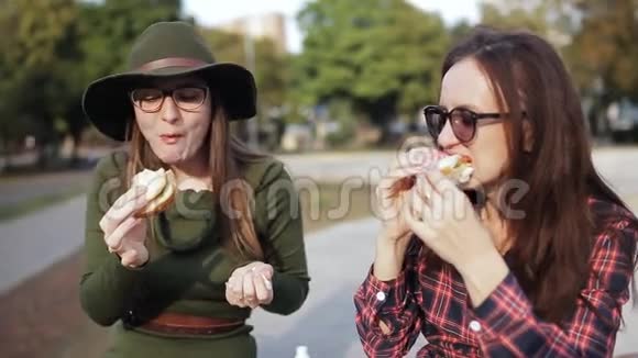 两个女孩在公园里吃三明治笑着说话呆在公园里假日三明治视频的预览图