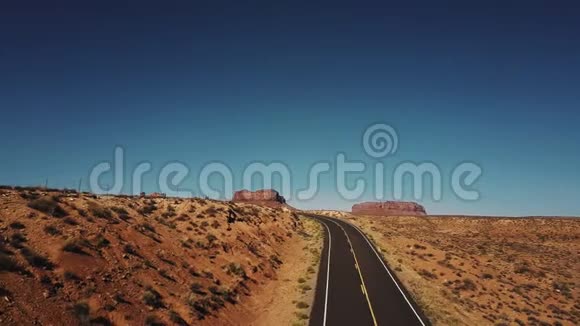 无人驾驶飞机在美国古迹谷的空旷沙漠道路和悬崖山的右侧飞行天空晴朗视频的预览图