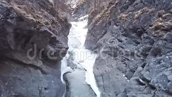 在雪覆盖的峡谷中飞行下面是河流原始的冬季景观和雪在岩石和周围飞视频的预览图