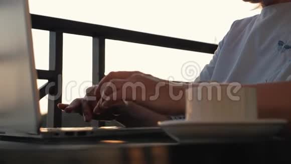 太阳下山时一个女孩正在桌子旁用笔记本电脑和一杯咖啡工作视频的预览图