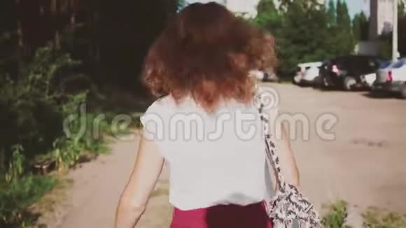 快乐的女孩走在他身后那个棕色头发的女孩在阳光明媚的一天散步视频的预览图