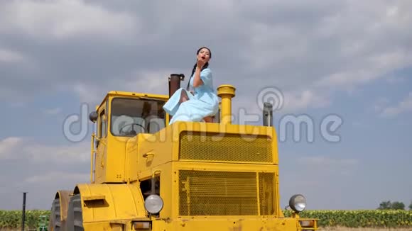 有魅力的女孩在蓝色的背景下在黄色的农业机器上缓慢地跳舞视频的预览图