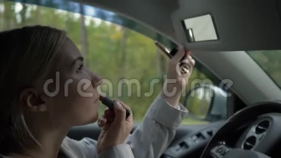 年轻的金发女人在车里画她的嘴唇视频的预览图