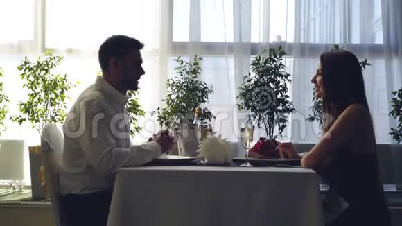 这对年轻夫妇坐在餐厅的桌子旁手牵手聊天浪漫关系视频的预览图