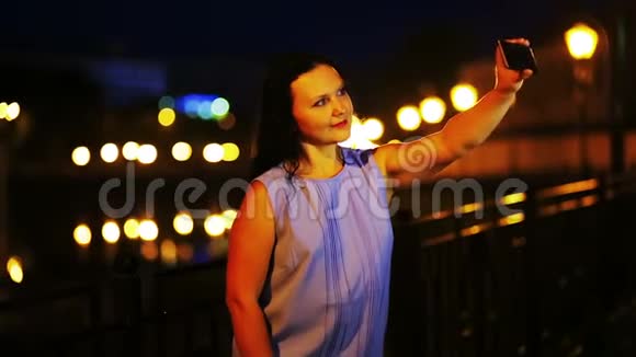 年轻的微笑女人在夜空的背景下在手机上自拍视频的预览图