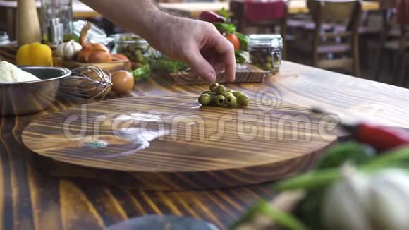厨师用刀子在木桌上切绿色橄榄男性手切橄榄做地中海沙拉织品视频的预览图