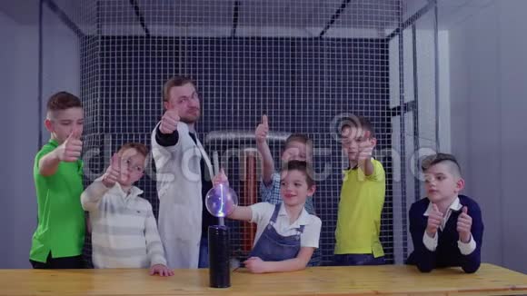 孩子们和老师用大拇指在特斯拉线圈上举着玻璃球视频的预览图