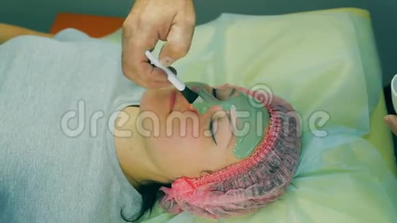 化妆师的男人的手在女人的脸上放了一个液体绿色的面具借助刷子视频的预览图