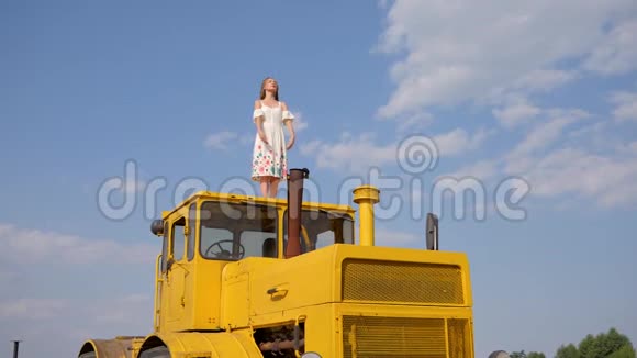 身着礼服的女性举手站在背景蓝天白云上的农业机器上视频的预览图