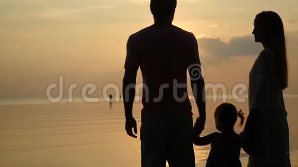 日落时分幸福家庭的剪影父亲母亲和女儿爸爸和妈妈女儿的手慢动作视频的预览图