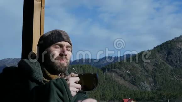 寂寞的胡须男站在观察甲板上看着一座山喝着大杯子里的咖啡或茶慢慢慢慢视频的预览图