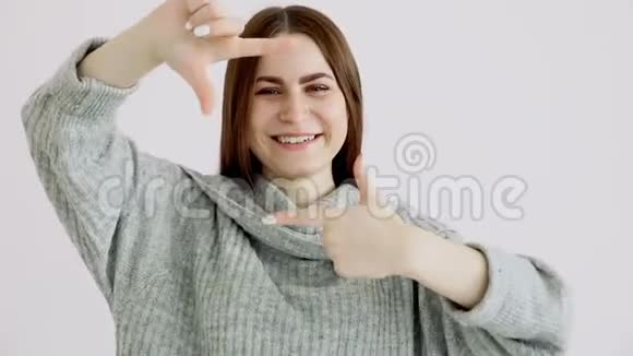 美丽的欧洲女孩穿着一件温暖的毛衣正对着白色的墙摆姿势欢笑和拍照视频的预览图