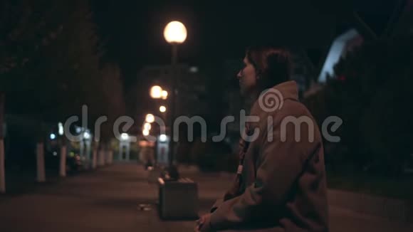 疲惫的女孩穿着米色外套头发破烂下班后走在黑暗的街道上视频的预览图