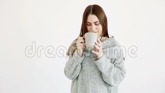 美丽的欧洲女孩穿着温暖的毛衣喝着白墙旁的热茶视频的预览图