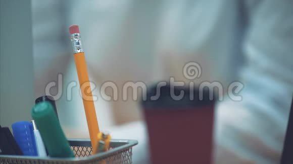 桌子上钢笔铅笔记号笔的特写在这个模糊的年轻商务女性为笔记本电脑工作过了一会儿视频的预览图