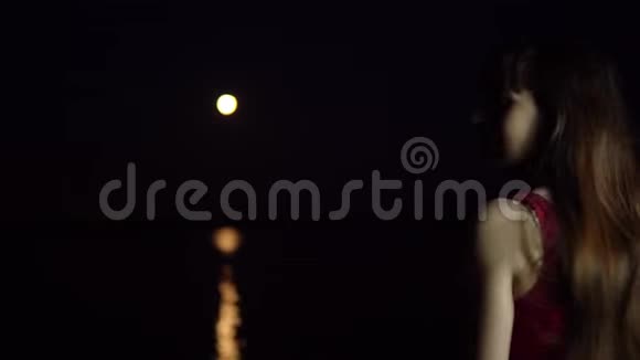 一个黑发的年轻女子欣赏河中倒影的红月视频的预览图