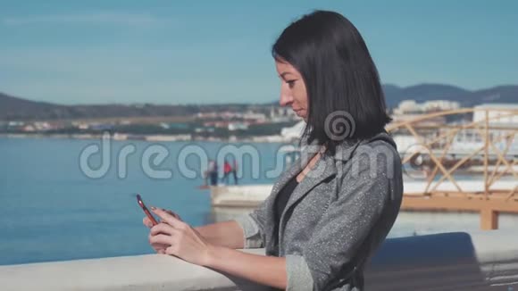 美丽的女人在海滩上使用手机年轻女性在户外智能手机上发短信的画像视频的预览图