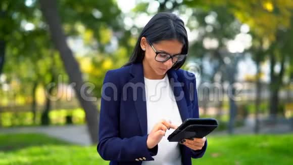 成功的商业女性与平板电脑在绿色公园背景穿正装戴眼镜的漂亮女孩视频的预览图