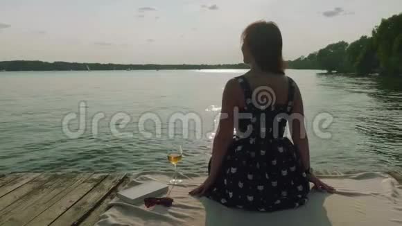 坐在老码头上的女人的后景女人拿了一杯白葡萄酒喝了它然后把它放回原处视频的预览图